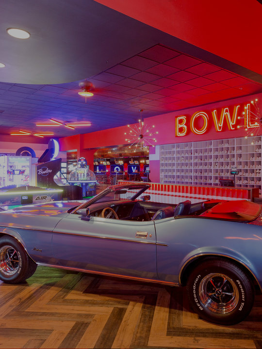 Blue vintage car inside a bowling alley with an arcade in the background