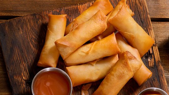 Veggie spring rolls with dipping sauce on a wooden serving tray