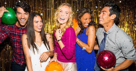Group of 5 young adults with bowling balls, smiling in front of a glitter background