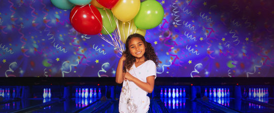 girl holding balloons in front of bowling lanes