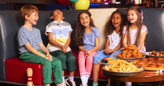 5 kids sitting on the couch laughing. Table next to them has a spread of food items. 