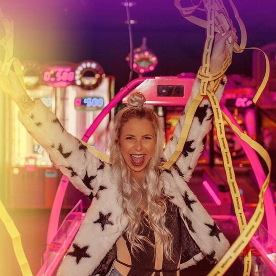 Teenage girl at arcade holding up winning tickets and smiling