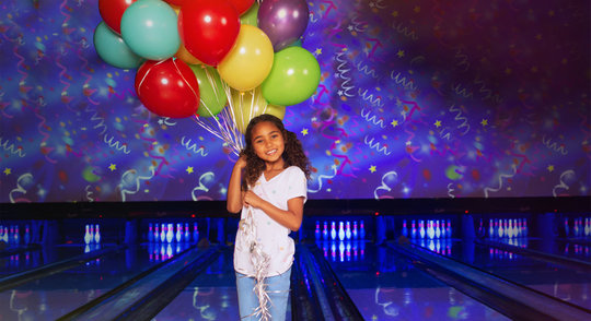 little girl holding balloons standing in front of lanes