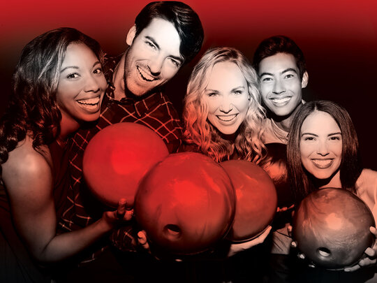 5 bowlers holding up bowling balls and smiling