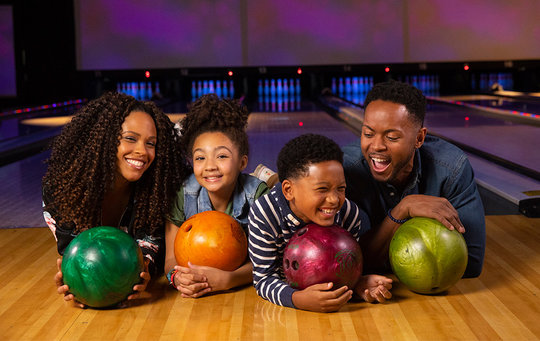 Family laying on floor holding bowling balls and smiling