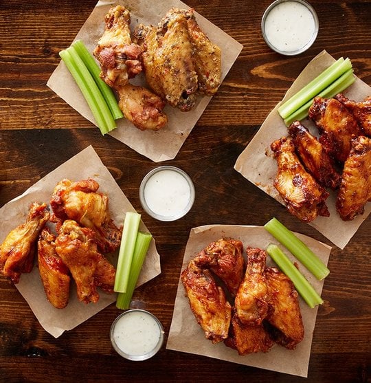 Four portions of chicken wings with different sauces and celery