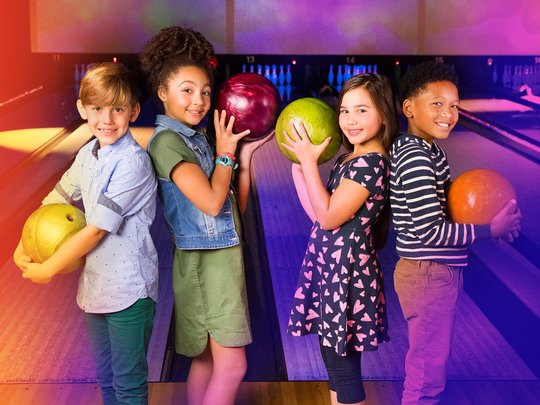 kids holding bowling balls in front lanes