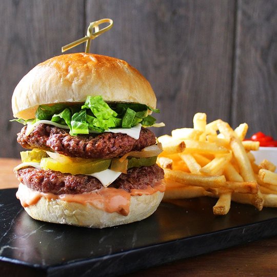 Double patty hamburger with sauce, lettuce, pickles and cheese. Fries to the right.