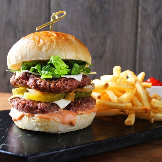 Double patty hamburger with sauce, lettuce, pickles and cheese.  Fries to the right.