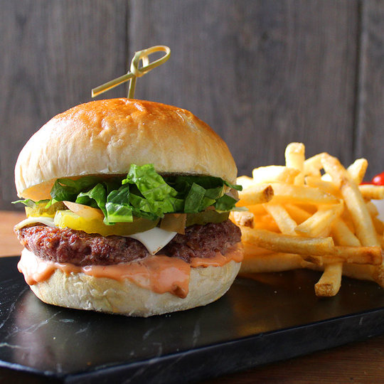 Hamburger with sauce, lettuce, pickles and cheese. Fries to the right.