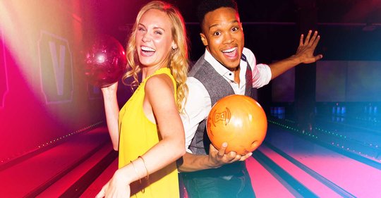 Two people holding bowling balls in front of lanes