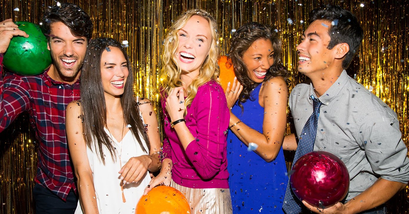 Group of 5 young adults with bowling balls, smiling in front of a glitter background