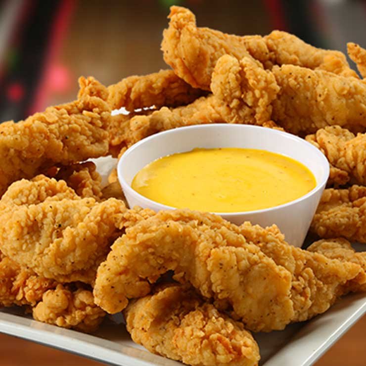 Chicken tenders on a plate around a cup of honey mustard sauce