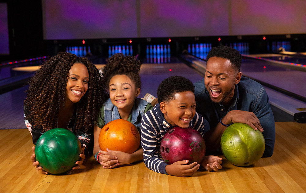 Family laying on floor holding bowling balls and smiling