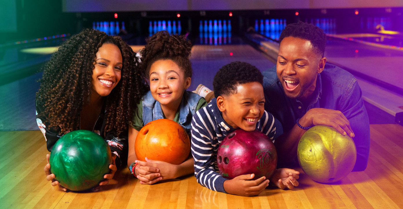Family laying down on the lanes holding bowling balls