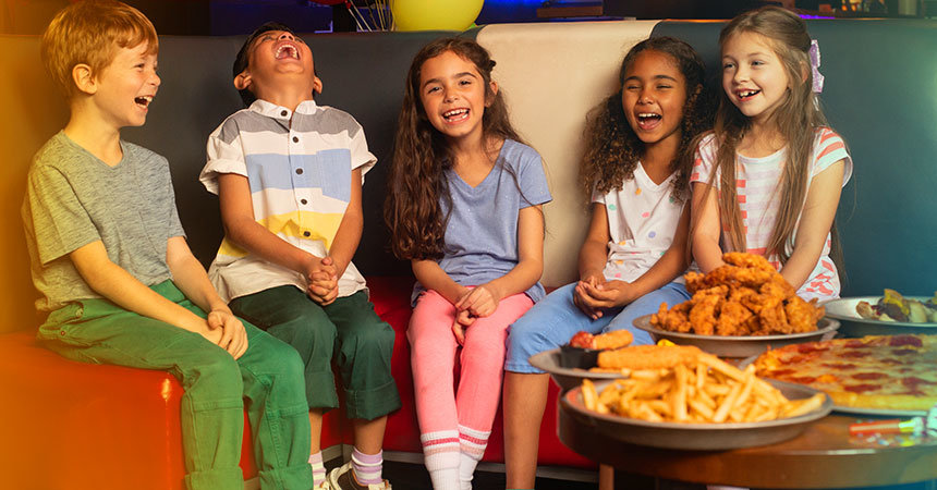 kids sitting on couch next to a table with pizza, wings, and French fries