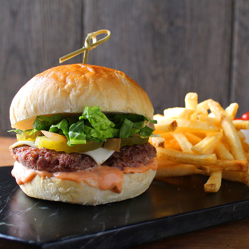 Hamburger with sauce, lettuce, pickles and cheese. Fries to the right.